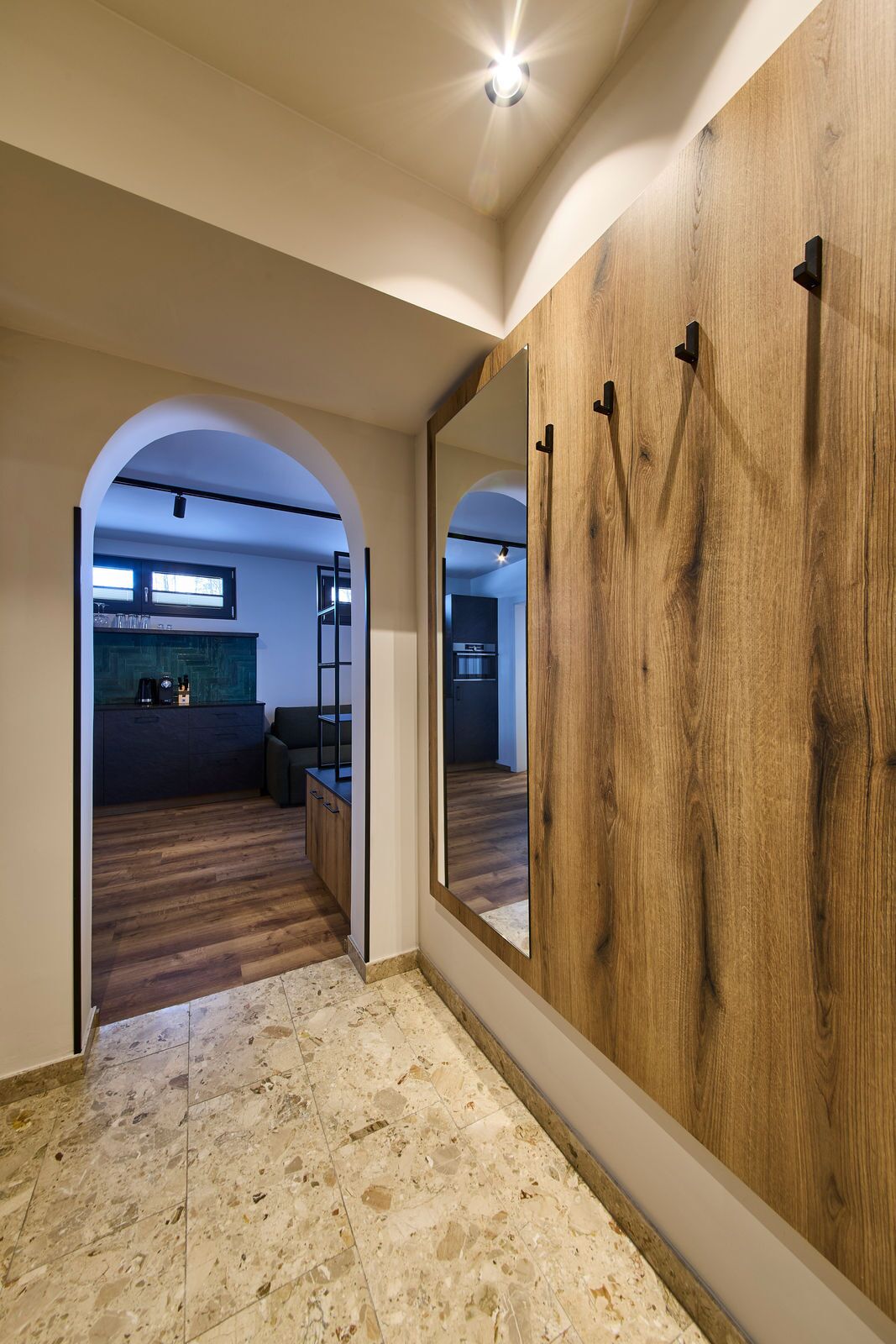 A hallway with a wooden wardrobe, a mirror, and a kitchen area visible through an archway.