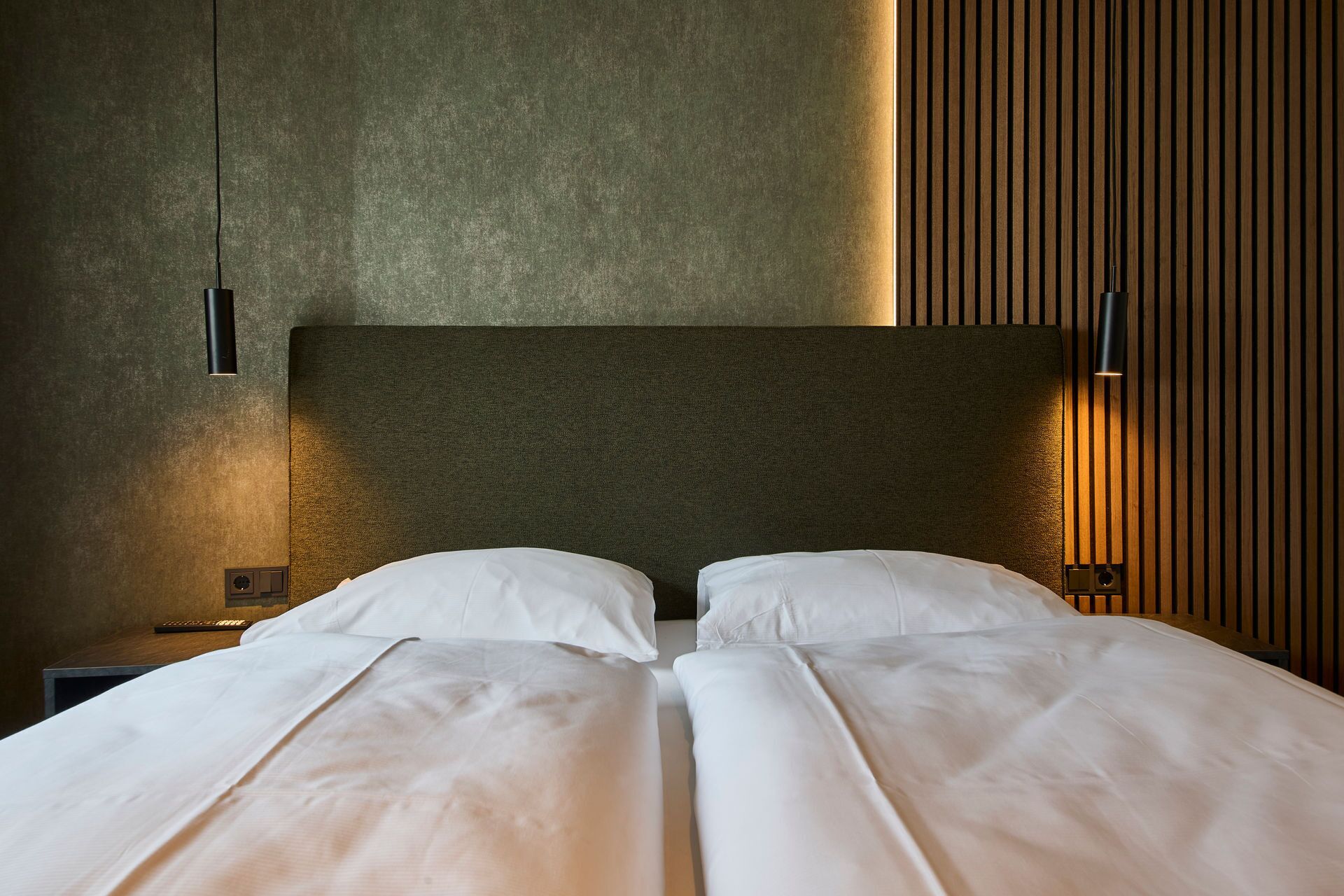A double bed with white linens, a textured wall, and a wooden panel on the right.