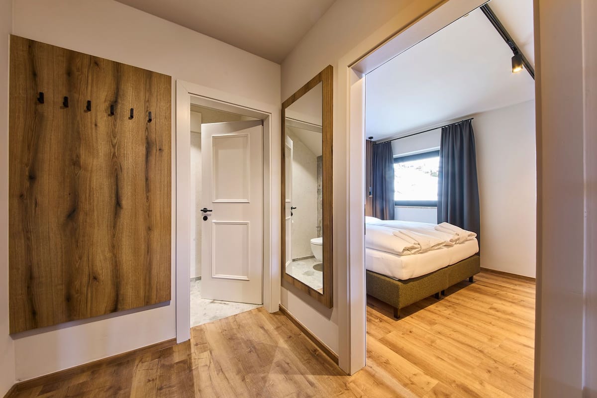 Une chambre d’hôtel avec une armoire en bois, un grand miroir, un lit avec un matelas et des oreillers, et une fenêtre avec des rideaux.