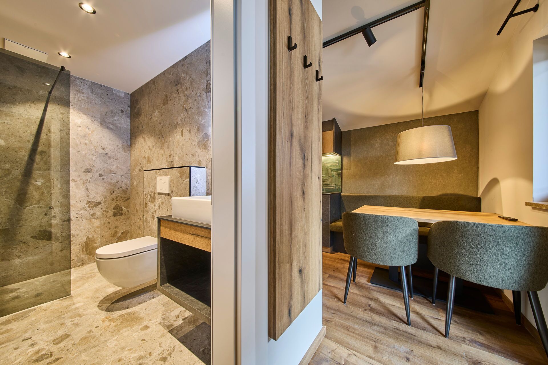 Un baño moderno con inodoro, lavabo y ducha. Se observa un panel de pared de madera con un espejo y una lámpara colgante.