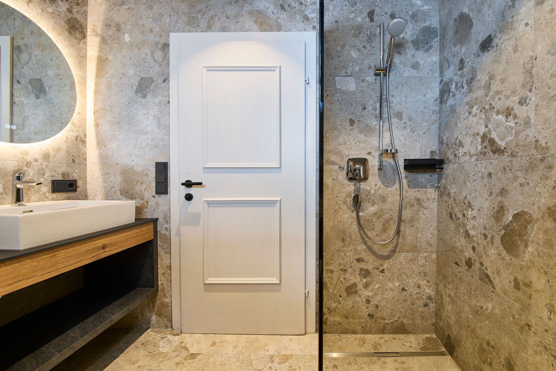 A bathroom with a white door, a sink, a mirror, and a shower with a handheld showerhead.