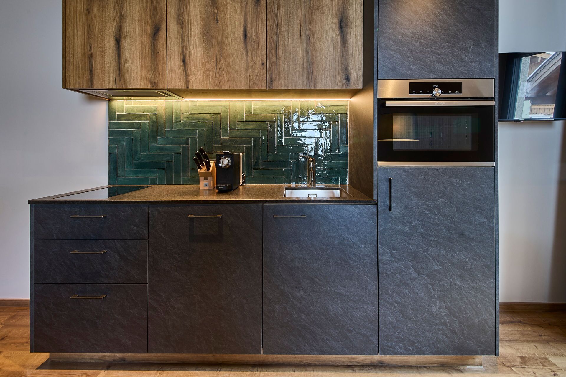 A modern kitchen with dark cabinetry, a herringbone backsplash, and a built-in oven.