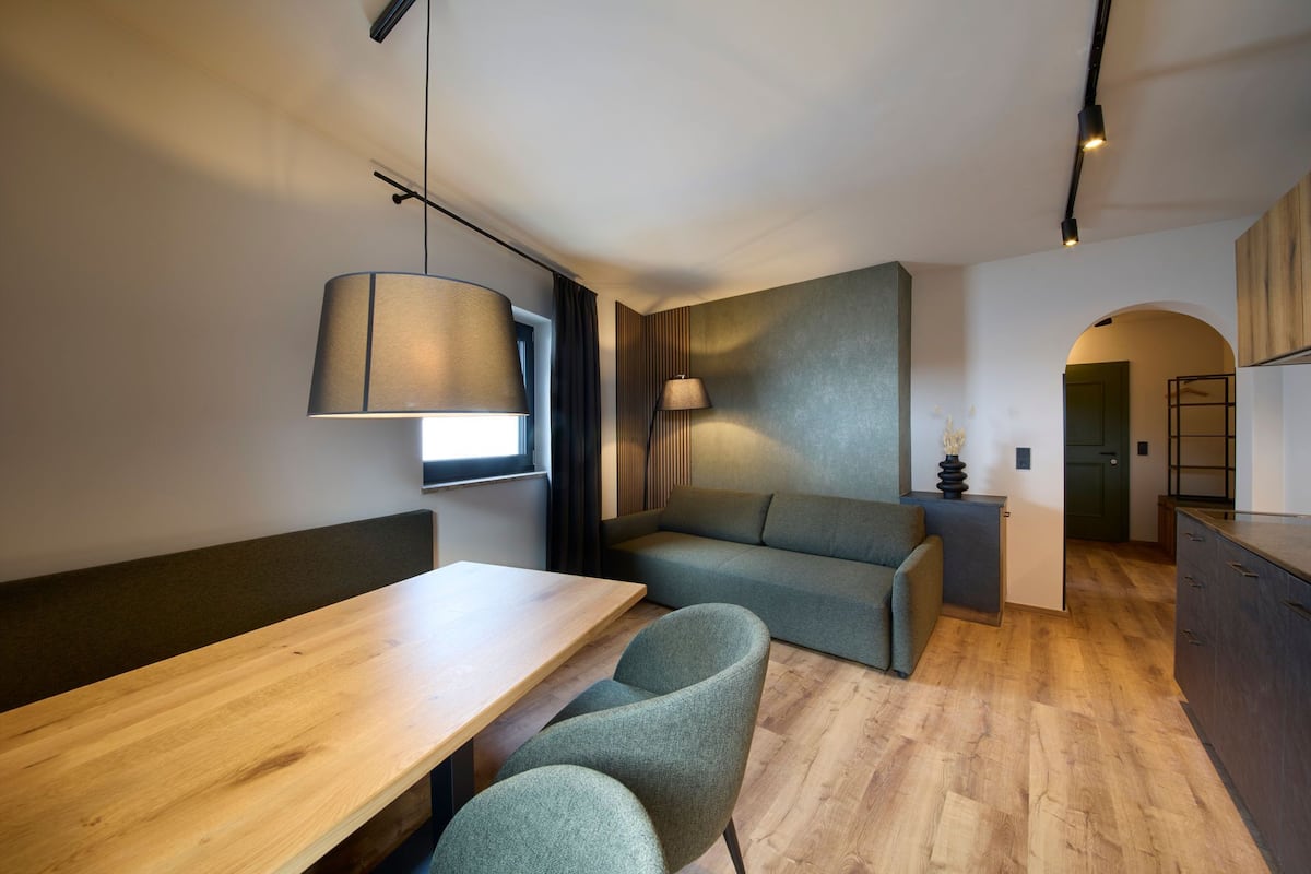 Un espace de vie moderne et compact, comprenant une table à manger en bois, un canapé et une petite kitchenette.