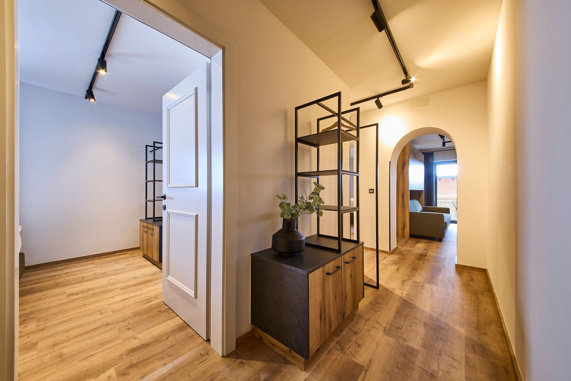 Um corredor moderno com piso de madeira, um console preto com uma planta e uma estante de metal.