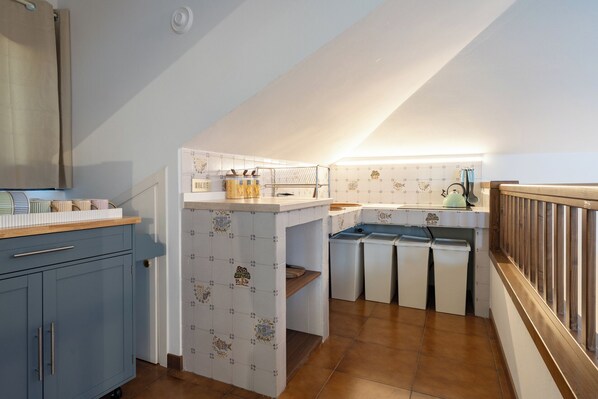A compact kitchen with a small island, a sink, and a stove. There are cabinets and a countertop with various kitchen items.