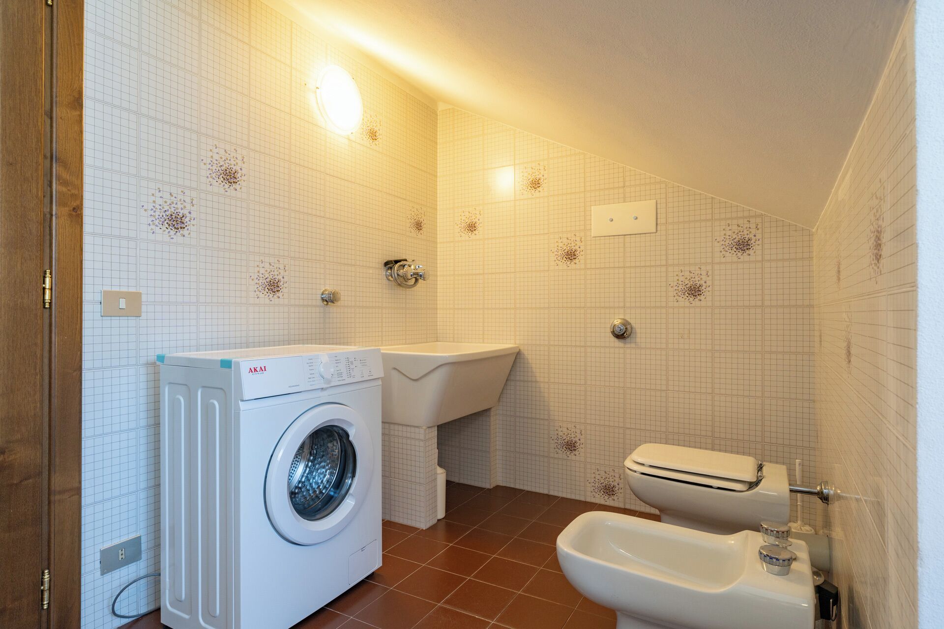A compact bathroom with a washing machine, toilet, and bidet.