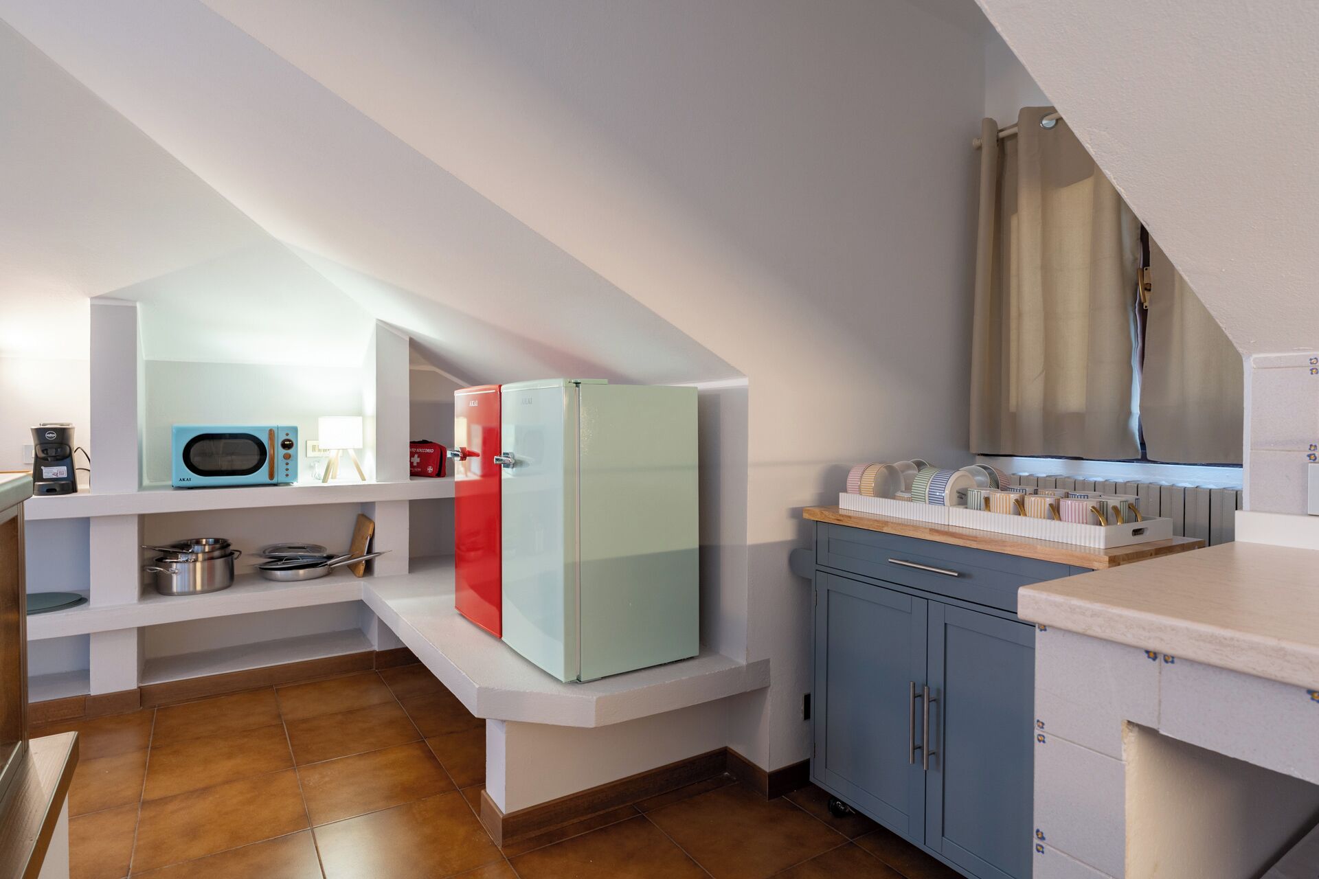 A compact kitchen with a microwave, a red refrigerator, and a coffee maker on a shelf.