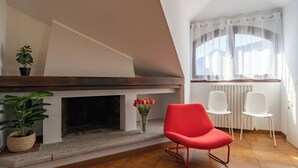A living room with a fireplace, a red chair, white chairs, and a view of the outdoors through a window. - La grande Valsassina - Loft (Pasturo)