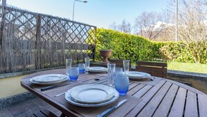 Mesa de madera preparada para comer al aire libre, con platos, vasos y cubiertos.