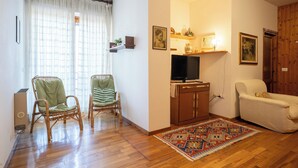 A living room with two wicker chairs, a sofa, a TV, and a patterned rug. - Maggio - appartamento con piscina (Cremeno)