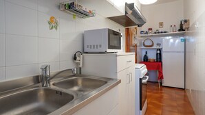 A kitchen with a stainless steel sink, a microwave, a refrigerator, and a red tablecloth-covered table. - Maggio - appartamento con piscina (Cremeno)