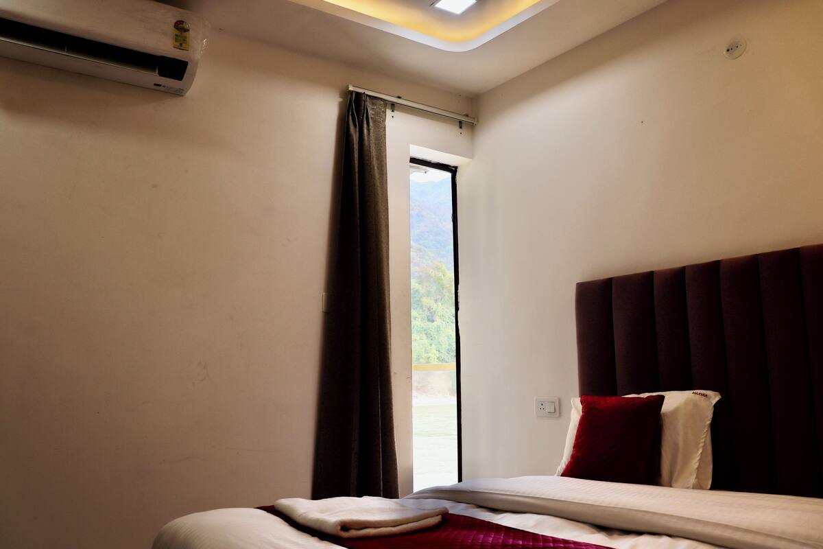 A bedroom with a bed, a window with curtains, a ceiling light, and an air conditioning unit.