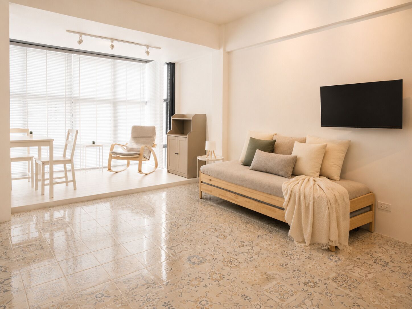 A modern living room with a sofa, a TV, a dining area with chairs, and a large window with blinds.