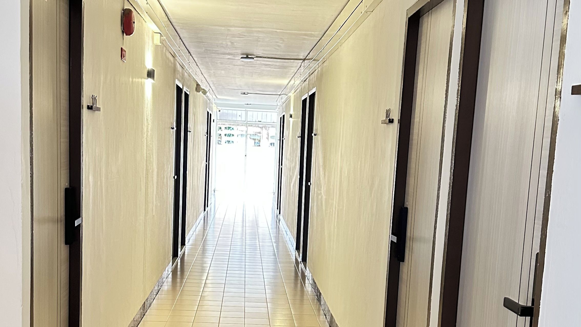A long, narrow hotel corridor with doors on both sides, leading to individual rooms.