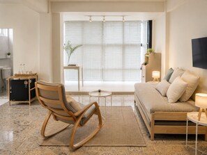 A modern living room with a sofa, a rocking chair, a small table, and a TV mounted on the wall. - 95 Lodge (Wang Thonglang)