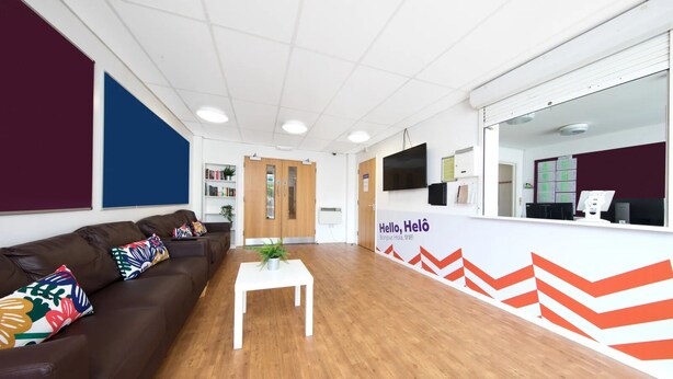 A reception area with a brown leather couch, a white coffee table, and a wall with a 'Hello, Helô' sign.
