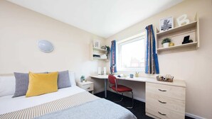A hotel room with a bed, a desk, a chair, a dresser, and a window with curtains.
