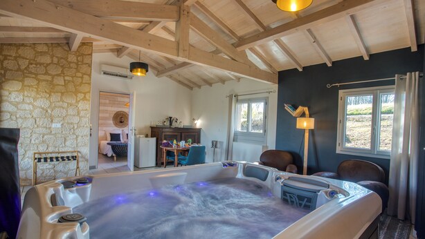Un espace de détente moderne doté d’un jacuzzi, de murs en pierre, de poutres en bois et offrant une vue sur l’extérieur.