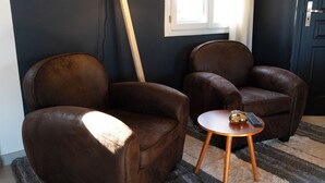 Une pièce comprenant deux fauteuils en cuir marron et une petite table d’appoint en bois, sur laquelle se trouvent une télécommande et un bol.