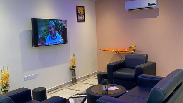 A modern living room with black leather sofas, a flat-screen TV, a ceiling fan, and an air conditioning unit. - Ekoara Apartments (Sekondi-Takoradi)