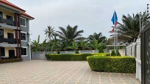 A courtyard with tiled flooring, palm trees, and a flagpole with a flag. - Ekoara Apartments (Sekondi-Takoradi)