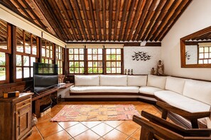 A living room with a wooden ceiling, a white sofa, a television, and a patterned rug. - Bz34 Casa 150m da praia Piscina e Sauna (Buzios)