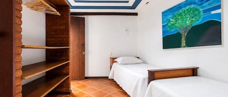 Un dormitorio con dos camas, una estantería de madera, un ventilador de techo y un cuadro de un árbol.