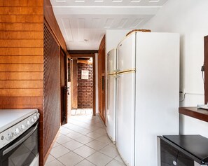 A kitchen with a stove, refrigerator, and wooden paneling. - Bz34 Casa 150m da praia Piscina e Sauna (Buzios)