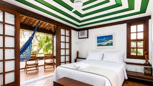 A hotel room with a bed, a hammock, a wooden chair, a small table, and a painting on the wall. - Bz34 Casa 150m da praia Piscina e Sauna (Buzios)