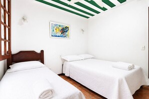 A room with two single beds, a wooden headboard, a painting on the wall, and a green ceiling.