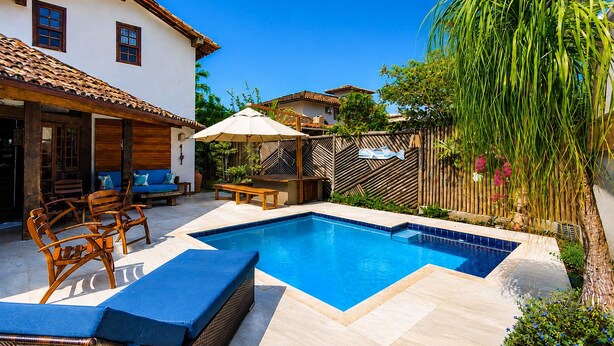 A swimming pool with a tiled deck, wooden furniture, and a bamboo fence. - Bz34 Casa 150m da praia Piscina e Sauna (Buzios)