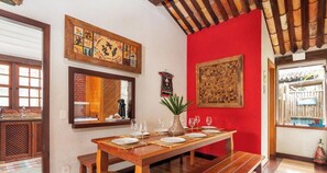 A dining area with a wooden table set for four, a vase, and a woven wall hanging. - Bz34 Casa 150m da praia Piscina e Sauna (Buzios)