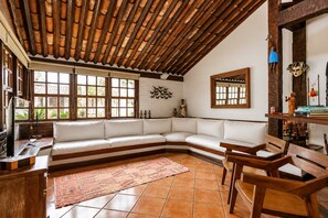 A cozy living room with a curved white sofa, wooden chairs, a tiled floor, and a wooden ceiling. - Bz34 Casa 150m da praia Piscina e Sauna (Buzios)