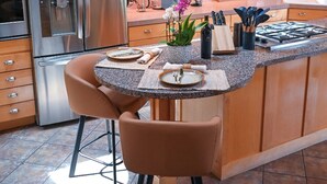 Een keuken met houten kasten, roestvrijstalen apparatuur, een granieten aanrechtblad met eiland en twee stoelen, en een spatwand.