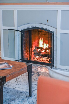 Ein Kamin mit Feuer, ein Holztisch und ein gemustertes Teppich.