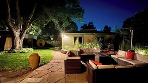 Een terras buiten met stenen vloer, rieten meubels en een grote plantenbak.