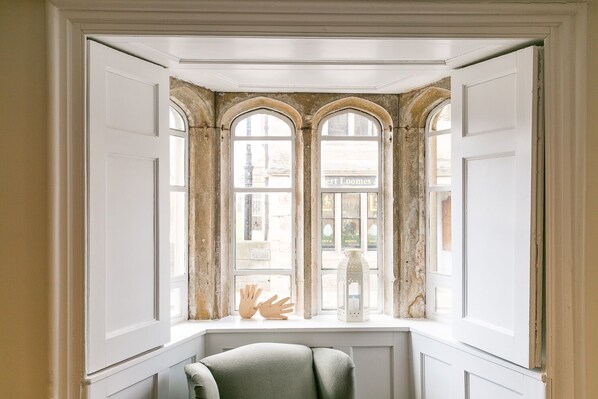 A room with a bay window, a chair, and a view of a street.