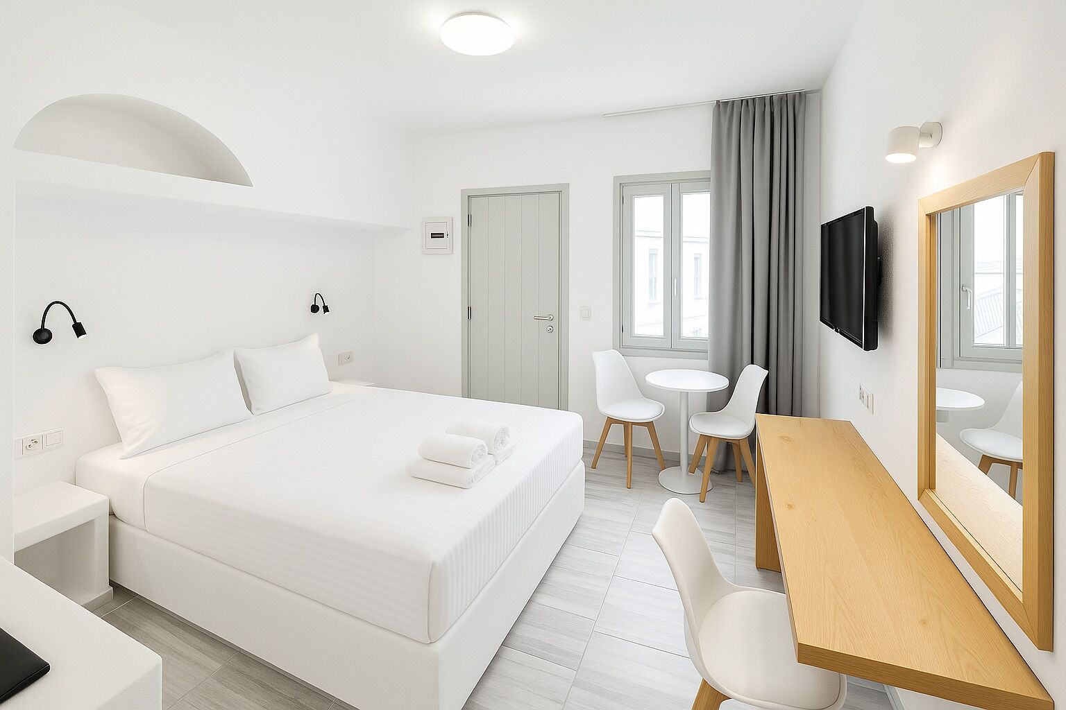 A modern hotel room with a large bed, a desk, two chairs, a TV, and a mirror.
