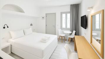 A modern hotel room with a large bed, a desk, two chairs, a TV, and a mirror.