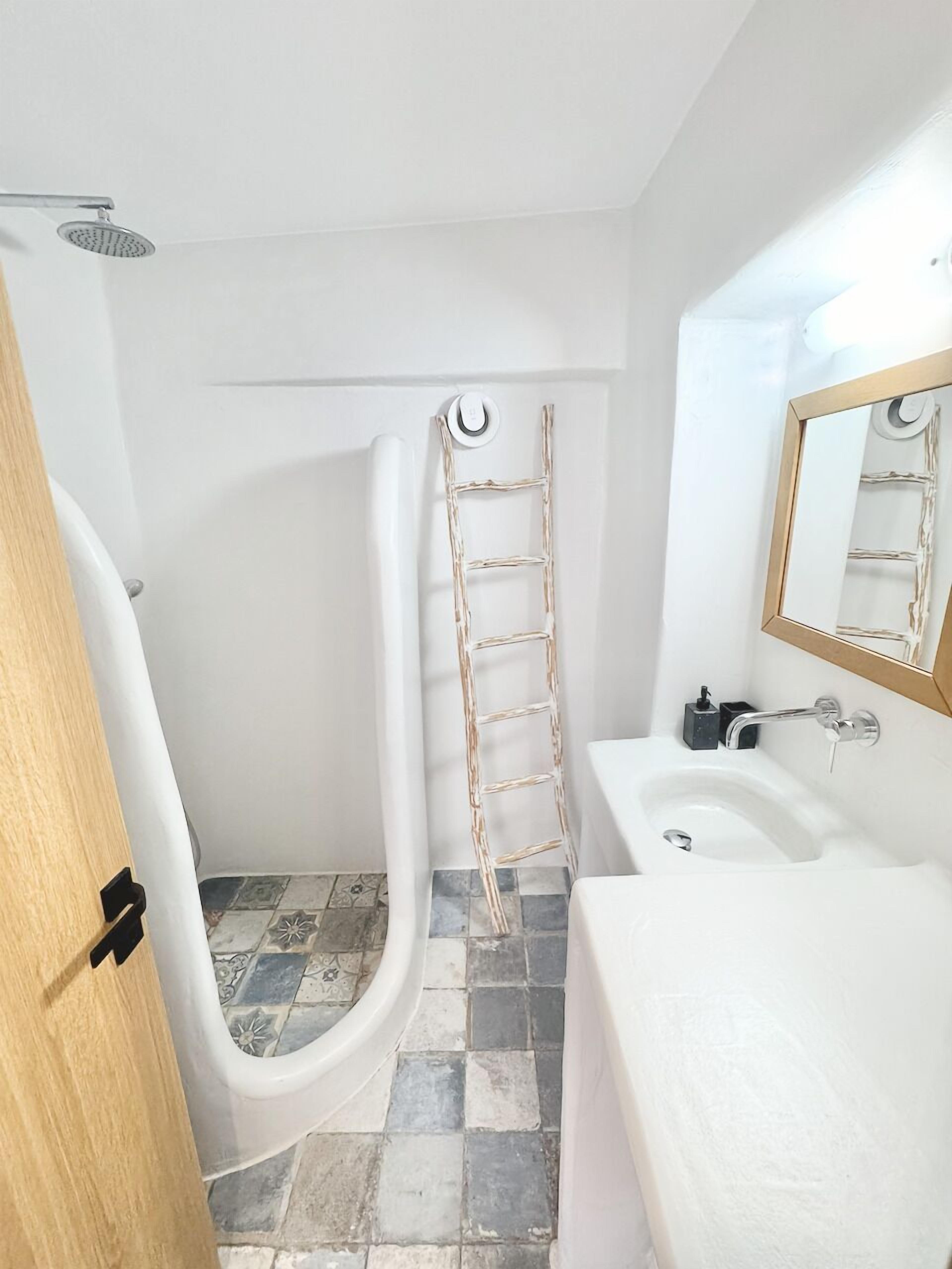 Ein Badezimmer mit einer weißen Badewanne, einem weißen Waschbecken, einer Holzleiter und einer Duschbrause.