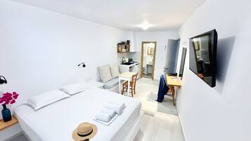 Ein modernes Hotelzimmer mit einem Bett, einem Schreibtisch, einem Stuhl, einem an der Wand befestigten Fernseher und einer kleinen Küchenzeile.