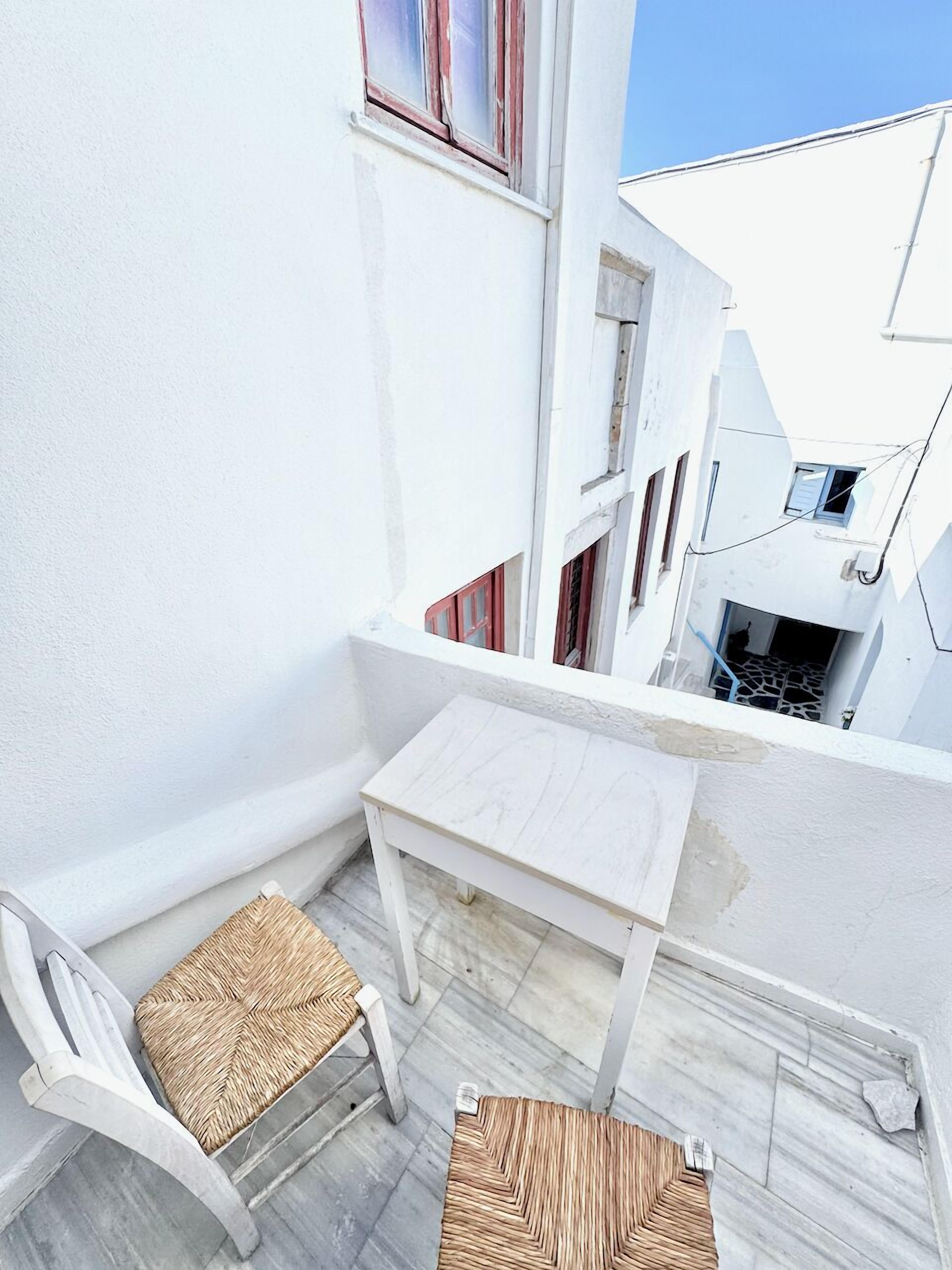 A small balcony with a white table and two wicker chairs.