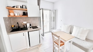 A compact kitchen with a sink, stove, and shelves, a small refrigerator, and a dining area with a table and chairs. - Castellino Naxos (Naxos)