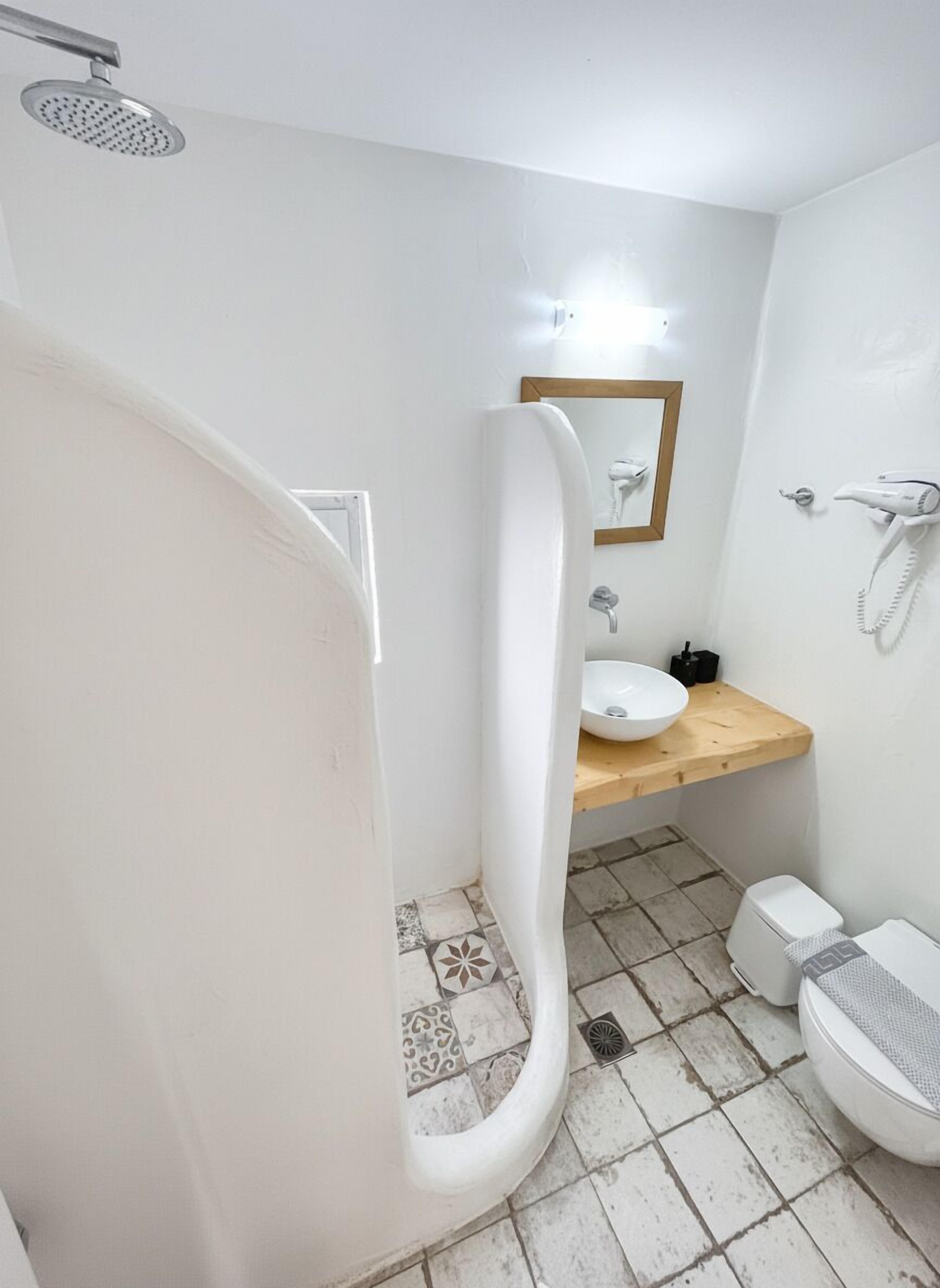 Een badkamer met een douche, wastafel, toilet en een haardroger aan de muur.