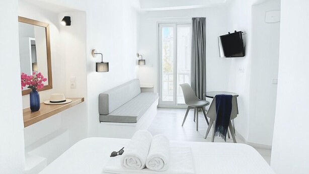 A modern hotel room with a large bed, a vanity with a mirror, a seating area, and a television on the wall. - Castellino Naxos (Naxos)