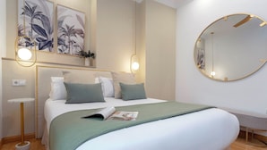 Une chambre d’hôtel bien rangée, avec un lit, une table de chevet, une lampe et un miroir rond accroché au mur.