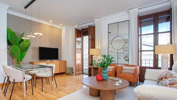Un salon moderne avec une table à manger en verre, des sièges confortables, un téléviseur à écran plat et une grande fenêtre agrémentée de rideaux.