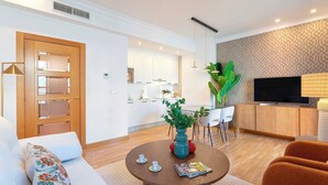 Un salon moderne comprenant un canapé, une table basse ronde avec un magazine, un téléviseur et un coin repas avec des chaises et une plante.