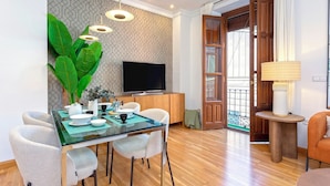 Un salon moderne avec une table à manger en verre, des sièges confortables, un téléviseur à écran plat et une grande plante.