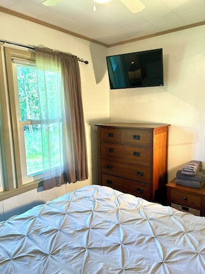 Una camera da letto con un letto, una cassettiera, una TV a parete e una finestra con tende.